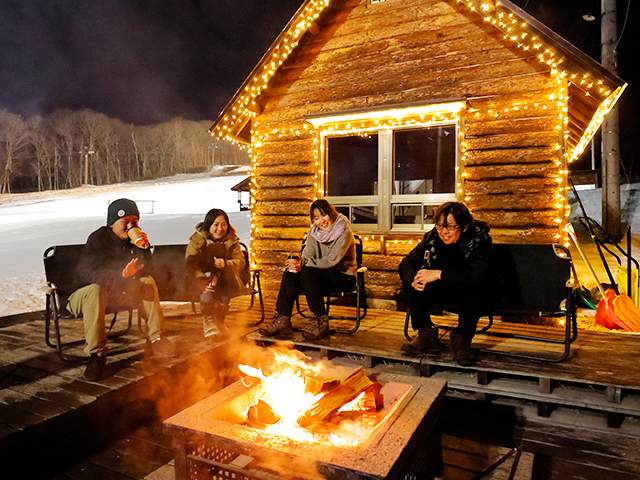 爺が岳スキー場中腹のログハウス前で焚き火を囲む人々、雪に覆われた夜のゲレンデ